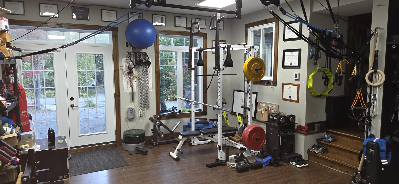 Studio privé S3 Training avec banc de musculation, poids et équipements de suspension près des grandes fenêtres.
