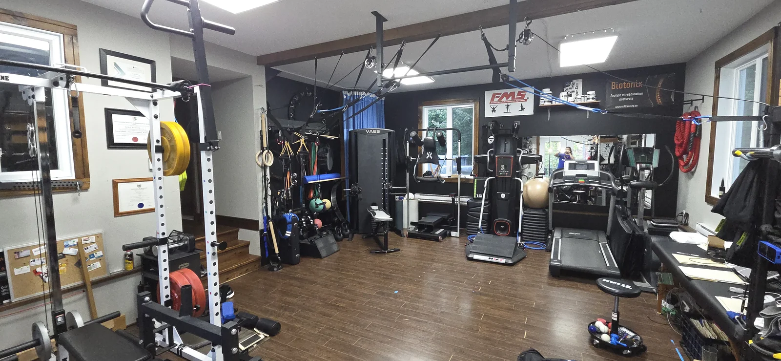 Vue du studio S3 Training avec mur noir, cage d’entraînement, sangles de suspension et équipements cardiovasculaires.